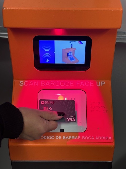 Photograph of a person holding a card against the bottom half of a white terminal with a screen on the top half and a red light overhead.