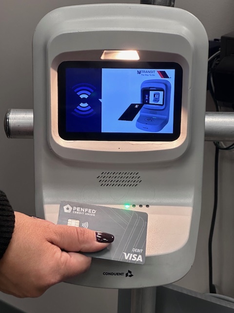 Photograph of a person holding a card against the bottom half of a white terminal with a screen on the top half and rounded corners